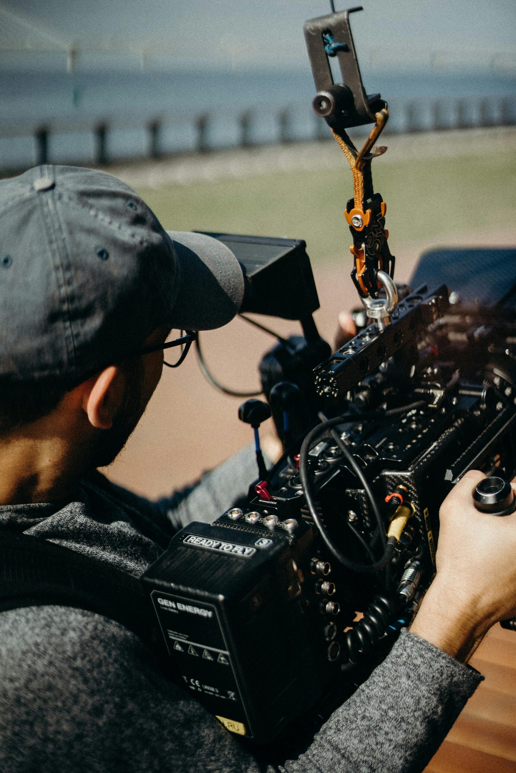 A man with a cap and eyeglasses operates a professional video camera during an outdoor shoot.