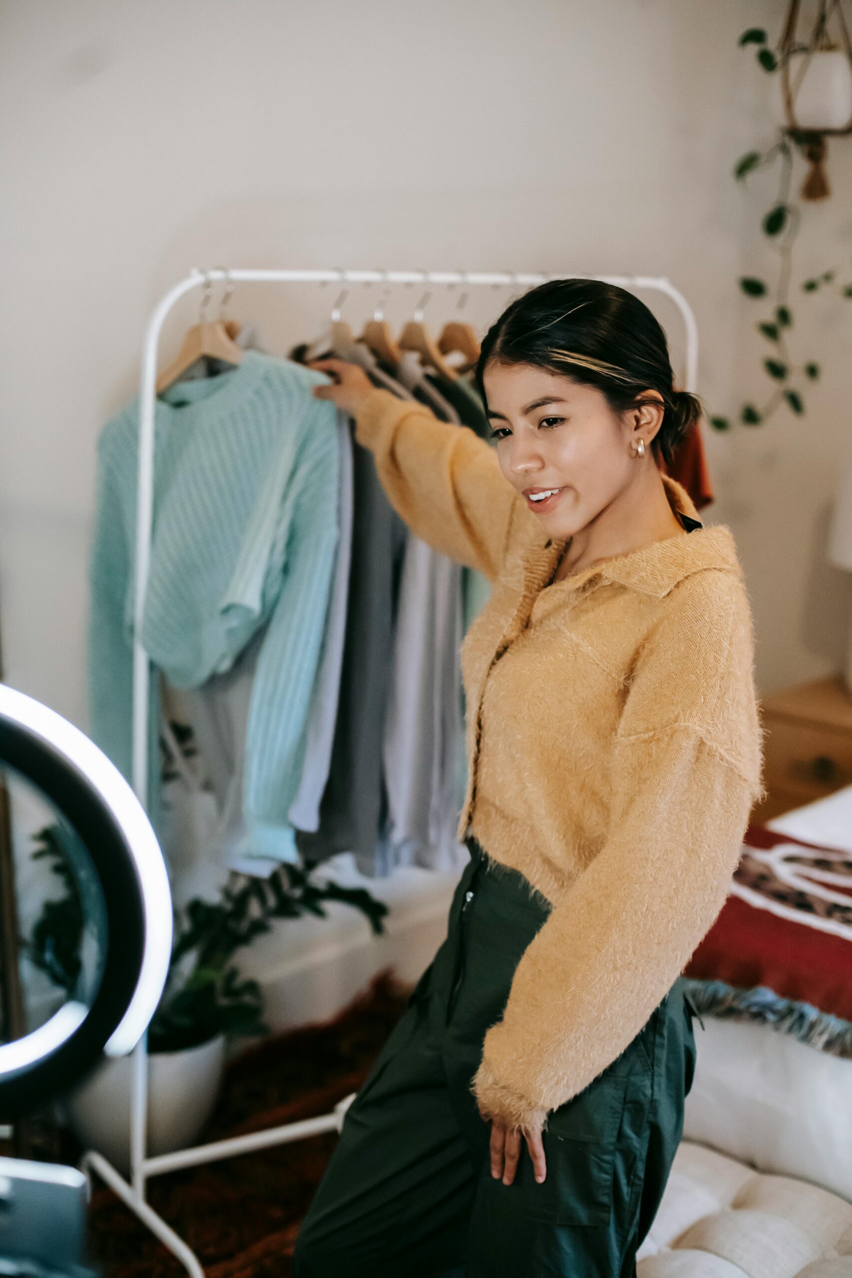 Young woman recording fashion content indoors with a smartphone and ring light.